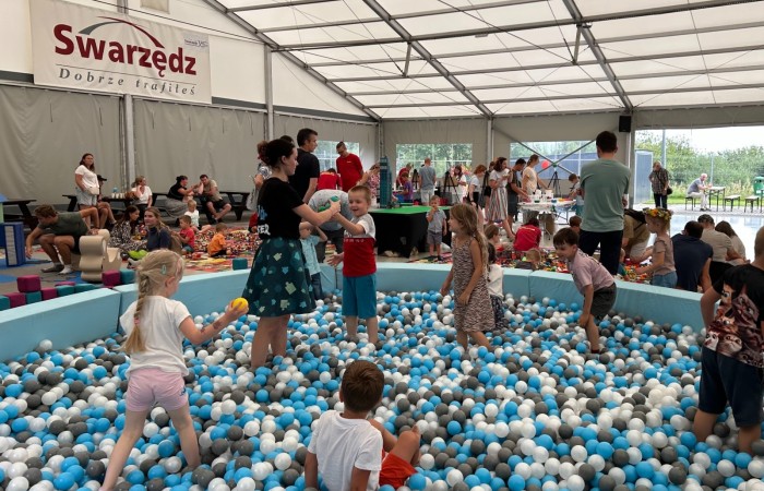 Piknik Trzech Pokoleń. Wnętrze namiotu przy scenie nad jeziorem. Na pierwszym planie widać wielki basen z kolorowymi kulkami, w którym bawią się dzieci. W tle widać innych uczestników pikniku, konstrukcję namiotu i jezioro Swarzędzkie.