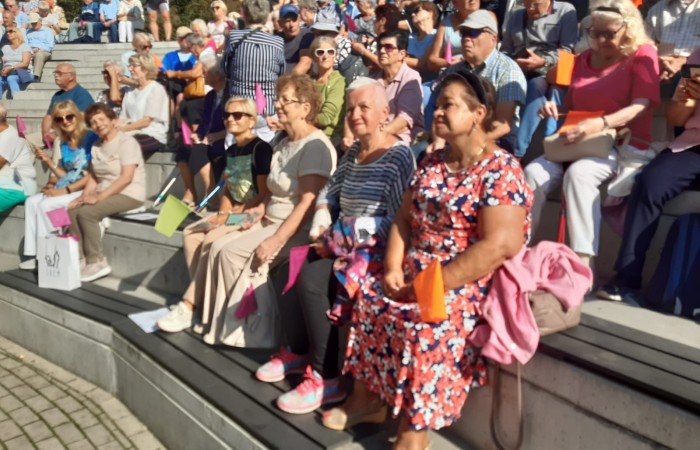 Widownia amfiteatru w Śremie. Na ławkach widać dziesiątki siedzących seniorów patrzących w kierunku sceny.