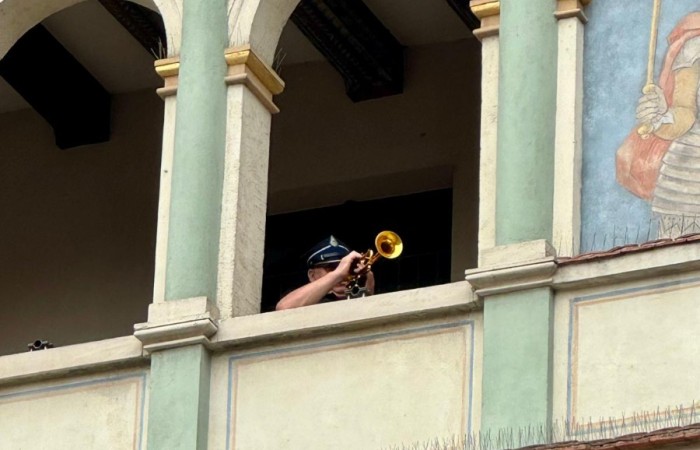 Zdjęcie wykonane w zbliżeniu. W jednym z prześwitów balkonu ratusza na Starym Rynku w Poznaniu widać trębacza grającego hejnał.