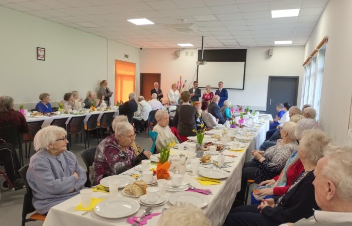 1. Podczas przedświątecznego spotkania z harcerzami w Dziennym Domu „Senior-WIGOR” seniorka i harcerka rozmawiają i uważnie się słuchają, siedząc blisko siebie. W tle inni seniorzy rozmawiają.