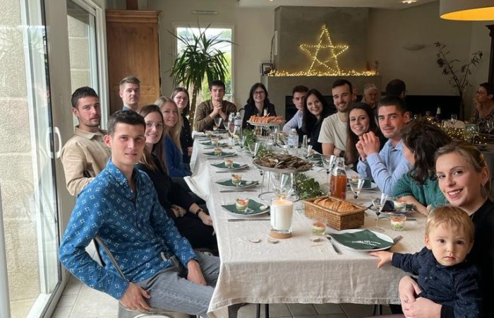 Na zdjęciu widać długi stół ubrany białym obrusem, przystrojony świątecznie. Stoją na nim świeca, talerze z przystawkami, lampki do wina, kosz z chlebem i dwie wysokie patery z owocami morza. Dookoła stołu siedzi 16 członków rodziny Żuljet wraz z nią. W tle na ścianie widać dużą świecącą gwiazdę ułożoną z lampek.